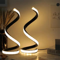 Two black spiral LED lamps glowing warm on a desk
